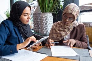 Young Muslim female private practice owners sitting in cafe, writing blog posts and using tablet for SEO on therapy websites. Simplified SEO Consulting can help your speech therapy website rank higher in search engines like Google and Bing!