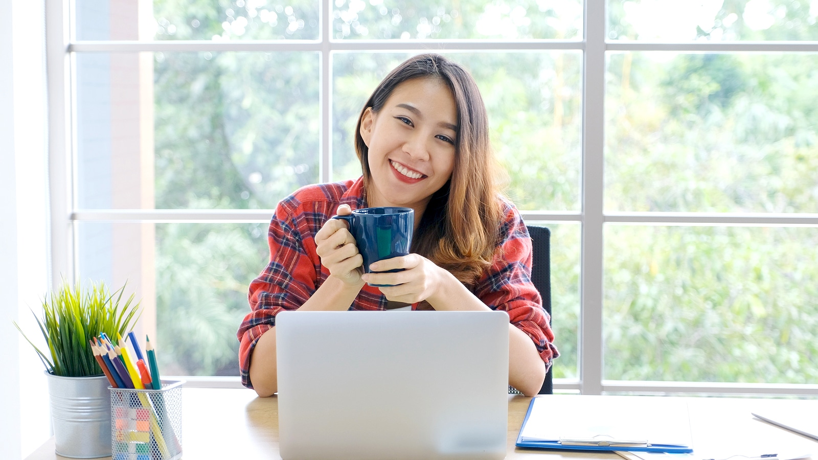 Happy woman working from home on her laptop drinking coffee. She works with an SEO specialist from Simplified SEO Consulting to rank better on Google