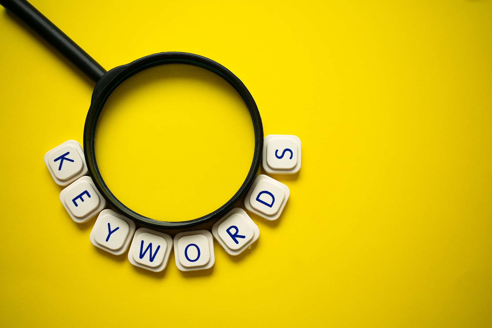 magnifying glass and letter tiles spelling "keywords" to represent the importance of business owners doing extensive keyword research when working on SEO