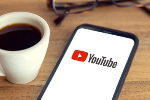 A close up of a phone with YouTube on the screen next to a cup of coffee. Contact Simplified SEO Consulting to learn more about SEO for therapists. You can learn SEO online to support your private practice today.
