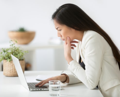 An Asian woman stands looking confused at her laptop. This could represent misunderstanding an off page SEO checklist. Learn more about on page and off page SEO, and how we can help with off page optimization.