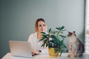 woman sits at her laptop next to her cat and smiles. She learned about blogging for SEO from a simplified seo specialist 