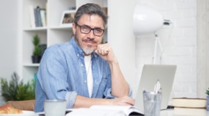 man with grey hair sits at his laptop and smiles at the camera representing copywriting for SEO and getting seo training with an seo specialist at simplified seo consulting