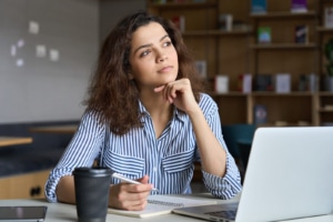 pensive woman writes in a notebook next to an open laptop representing copywriting for SEP. Learn how to optimize your website in SEO training with an SEO specialist