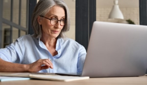 older woman types on her laptop. Perhaps she is a therapist learning how to blog for SEO. Learn how to draw inspiration from a copywriter and SEO expert at Simplified SEO Consulting