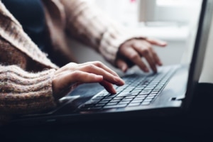 woman in a sweater types on a laptop representing blogging for SEO. Learn more from an seo expert and copywriter at Simplified SEO Consulting