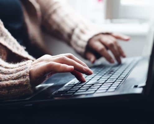 woman in a sweater types on a laptop representing blogging for SEO. Learn more from an seo expert and copywriter at Simplified SEO Consulting