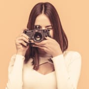 Image of a woman holding a camera as if she is taking a photo in front of a orange background. Private practice SEO can be difficult to navigate. Simplified SEO Consulting offer SEO help for therapists!