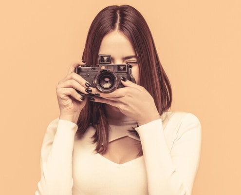 Image of a woman holding a camera as if she is taking a photo in front of a orange background. Private practice SEO can be difficult to navigate. Simplified SEO Consulting offer SEO help for therapists!