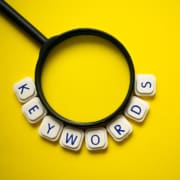 Photo of a magnifying glass with the word keyword spelled out underneath representing how mental health keywords can be used through blogging to improve SEO for therapists and counselors