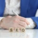 Image of SEO spelled out in blocks in front of someone wearing a suit. Simplified SEO Consulting specializes in mental health SEO. We give specialized and tailored search engine optimization for counselors. A part of this includes footer SEO. Call today to get a consultation.