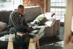 Photo of a man sitting on a couch using a computer. This photo represents how therapists can add mental health SEO keywords to their website through service pages and blogs.