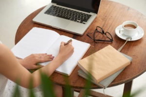 Image of a woman writing in a journal with a computer sitting in front of her. We provide help with SEO for mental health professionals. As a part of SEO for therapists, we suggest including an About the Auther section. Are you needing SEO for private practices? We can help, reach out now!