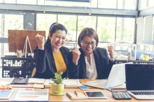 Photo of two women looking at a computer and smiling. Represents how seo consulting helps therapists decide what level of private practice SEO is right for them and their practice.