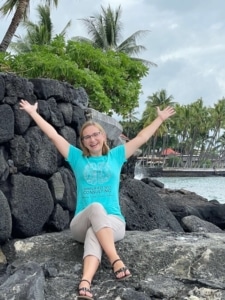 Jessica sitting on a lava rock in Hawaii by the ocean wearing her Simplified SEO Consulting tshirt. Join us for the global marketing experience cruise to Hawaii!