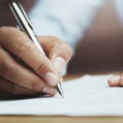 A picture of someone sitting at their desk and holding a pen in their right hand to write on a note book. This represents how you can write your blogs to boost your SEO with Simplified SEO Consulting