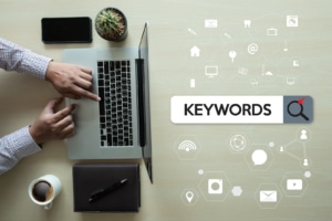 A close up of a person typing on a laptop with the term "keywords" shown nearby. Learn how Simplified can support counselor SEO. Contact us for SEO help for therapists.