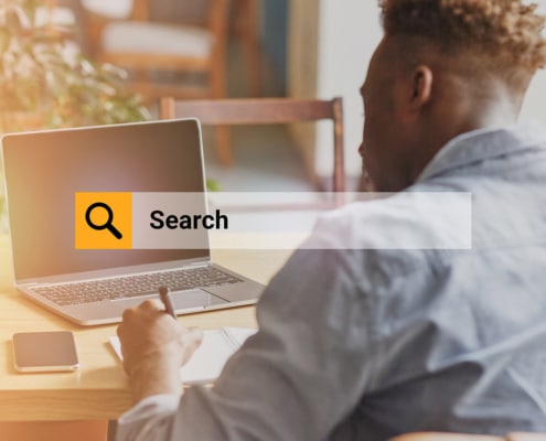 Image of a man at a laptop overlayed by an orange search bar. Which highlights the importance of knowing how to write a meta description for a private practice website. Especially for a therapists about page when it comes to their SEO.