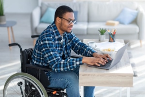 Image of a man in a blue shirt in a wheelchair typing at a computer. Showing the type of clients you can reach when you invest in SEO for therapists and mental health professionals. Where you can learn to where to use keywords within your meta description on your about page.