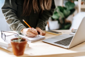 Photo of a woman writing something in a notebook at her desk. If your looking to begin attracting your ideal clients, discover how creating high quality content can help you.