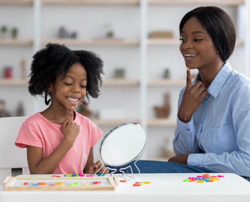 Photo of a female, black speech therapist helping a young girl with articulation using a mirror. This represents the important work SLPs in private practice do. SEO can help get your services out to move potential patients.