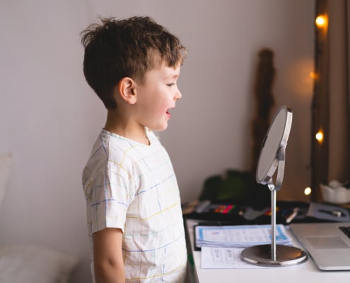 Photo of small boy looking at mirror representing a boy who's pediatric speech therapist has done excellent keyword research and used both long tail keywords and short tail keywords as part of their overall SEO strategy.