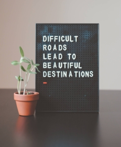 Shows a sign that says "Difficult Roads Lead to Beautiful Destinations". Represents how seo for mental health professionals can help individuals find the help they need during the summer.