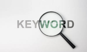 Shows the word "Keyword" with a magnifying glass over it. Represents how seo for mental health supports using keywords on both your website and social media.