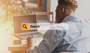 A person writes in a notebook while a search bar appears over his laptop. Learn how to support local SEO for therapists by searching for therapist directories today.