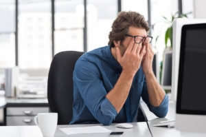 A man sitting at his desk frustrated and holding his face. Don't let blogging for your private practice ruin your day. Our SEO services for therapists and private practice owners can help you navigate through the challenges of writing. 