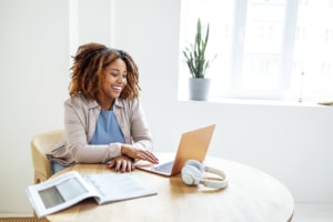 Photo of an African American woman smiling and working on her laptop. Discover how to help your private practice SEO with ensuring your content is easy to read for users visiting your website. Learn about readability here!