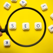 Letters spelling out SEO under a magnifying glass being held by a hand. Looking to understand SEO better? We can teach you about Local SEO for therapists and how to find your ideal client.