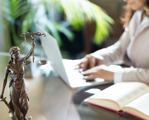 Lady Justice on a desk with individual typing on a laptop. We are here to help your law firm grow with SEO techniques. Learn more about SEO keywords and ads here.