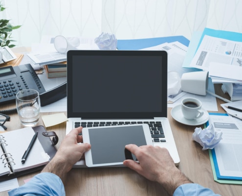 A person touching a tablet sitting on a laptop with papers on a desk. Searching for how you can improve your SEO in healthcare? We can teach you how to make SEO for the healthcare industry benefit you.