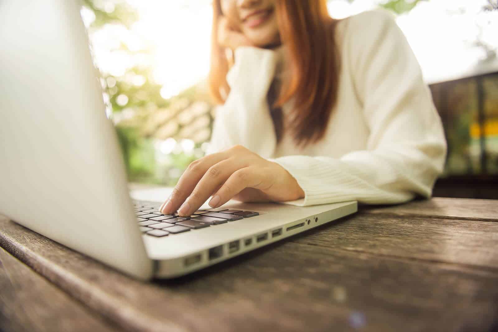 Image of a woman siting at a table smiling and working on her laptop. Learn the basic principles to SEO for mental health therapist to helping your website rank and finding your ideal clients.