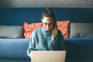 Image of a smiling woman wearing a gray sweater sitting on the floor using a laptop. Discover how Simplified SEO Consulting can help you as a private practice owner work on your private practice SEO.