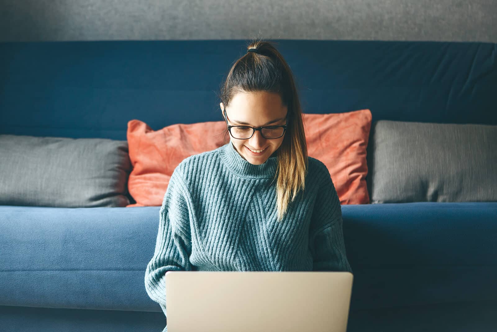 A woman sits on the floor with her back on couch while working on her laptop. Trying to understand DIY SEO for small business owners? DIY SEO can be taught by our experienced SEO specialists so you can implement it on your own.