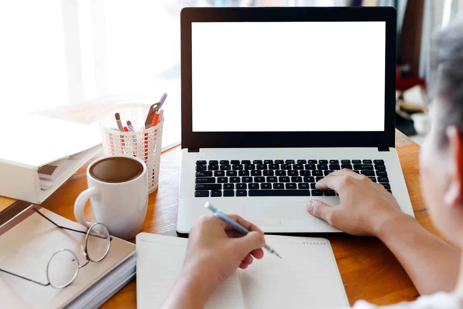 Image of a person using a laptop with a white screen and taking notes. Discover how you can begin using niche keywords to help with your private practice SEO here!