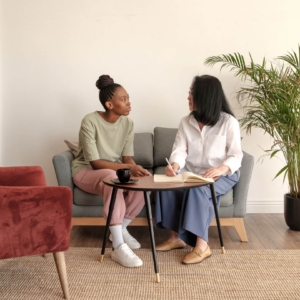 Shows a young, black female talking to her therapist in a modern chic office. Represents how digital marketing for therapists can help therapy websites with seo for therapists and seo keywords for mental health.