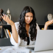 Shows a black, female therapist looking confused with her hands up and looking at her laptop. Represents how therapist seo can help therapy websites.