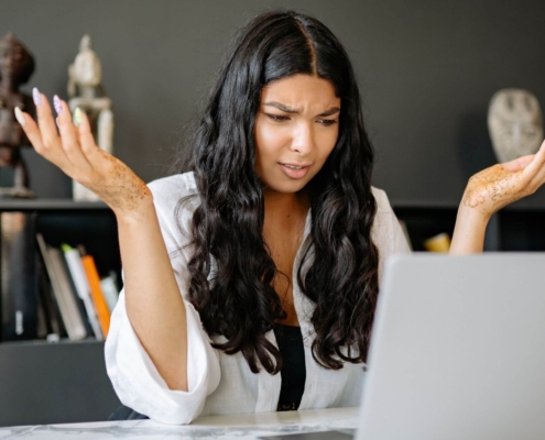 Shows a black, female therapist looking confused with her hands up and looking at her laptop. Represents how therapist seo can help therapy websites.