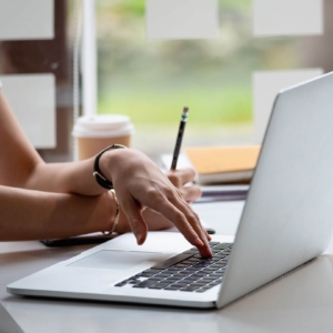 Shows someone typing on their computer with left hand while holding a pencil with their right hand. Represents how seo for online counseling can be boosted by using Tips for Copywriting Efficiently Without AI.