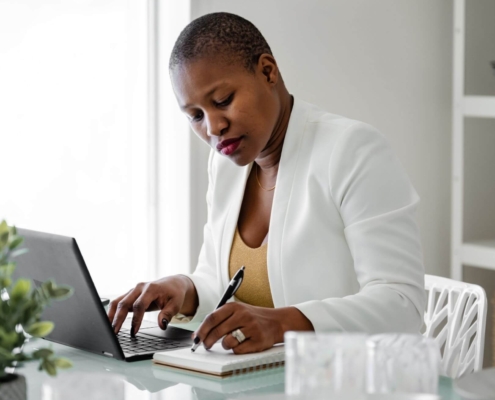 Shows a black, woman therapist taking notes with a pen and notepad while looking focused. Represents how you can not use copywriting ai tools and still implement private practice SEO.
