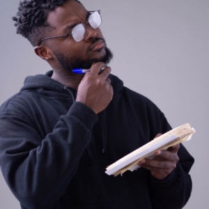 Shows a young, professional black man contemplating while holding a blue pen and a notebook. Represents how using counselor seo and search engine optimization for counselors to enhance your service page.