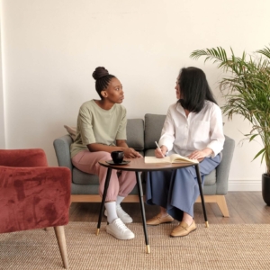 Shows a young black woman talking to a middle age therapist in her modern office. Represents how counselor seo and seo for online therapy can lead potential clients to you.