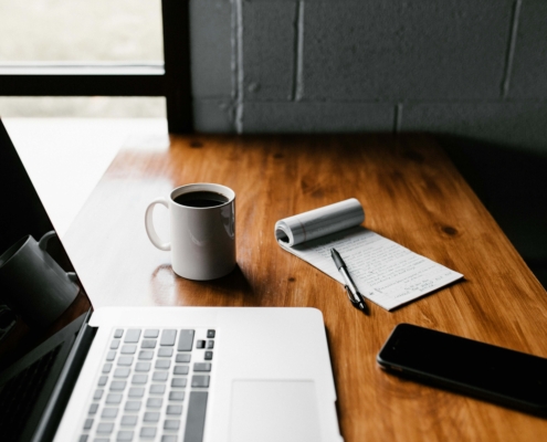 Image of a laptop, coffee mug, cell phone, and notepad sitting on a table. Learn how to effectively attract your ideal client and show up in search results by learning how to write a therapy blog for your SEO.
