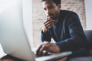 A black man sitting on a couch while typing on a laptop. To build ethical backlinks, consider writing a guest blog for a colleague. Start building your SEO today.