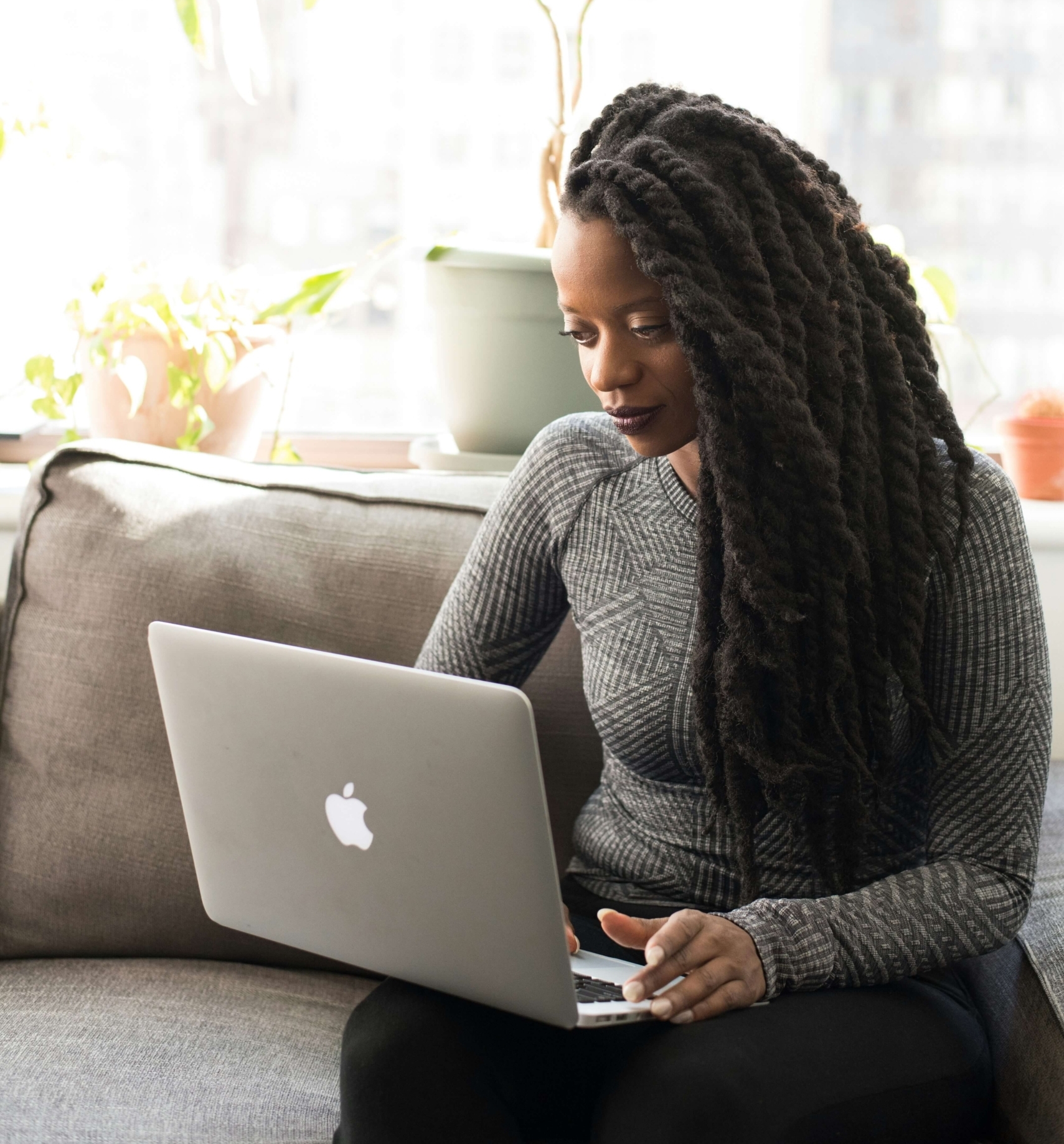 Image of an African American woman sitting on a couch holding a laptop. Discover how writing your therapy blog can help your SEO and find your ideal clients!