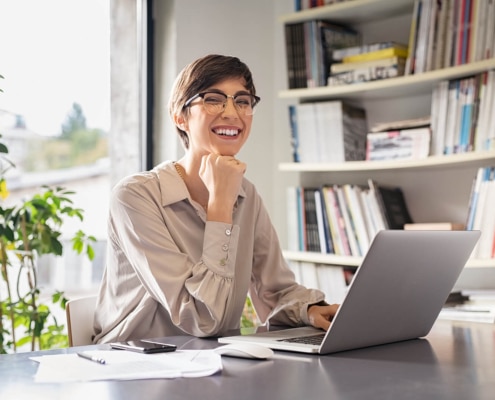 A young professional woman smiling while working on her laptop. Our SEO consulting services can help you reach new potential clients. Reach out today to start growing your online practice!