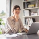A young professional woman smiling while working on her laptop. Our SEO consulting services can help you reach new potential clients. Reach out today to start growing your online practice!